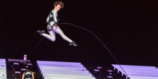aerialist jumps from the side of the building while the harness cord slacks in the air