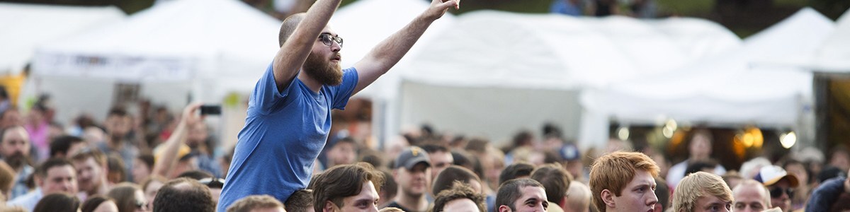 a crowd member sits on someone's shoulders during a concert in point state park